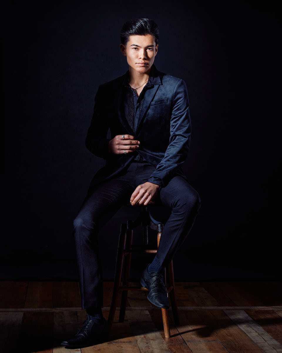 How to Become a Male Model in Chicago-Santiago sits confidently on a stool, slightly angled to the camera with one hand resting on his knee and the other adjusting his jacket.