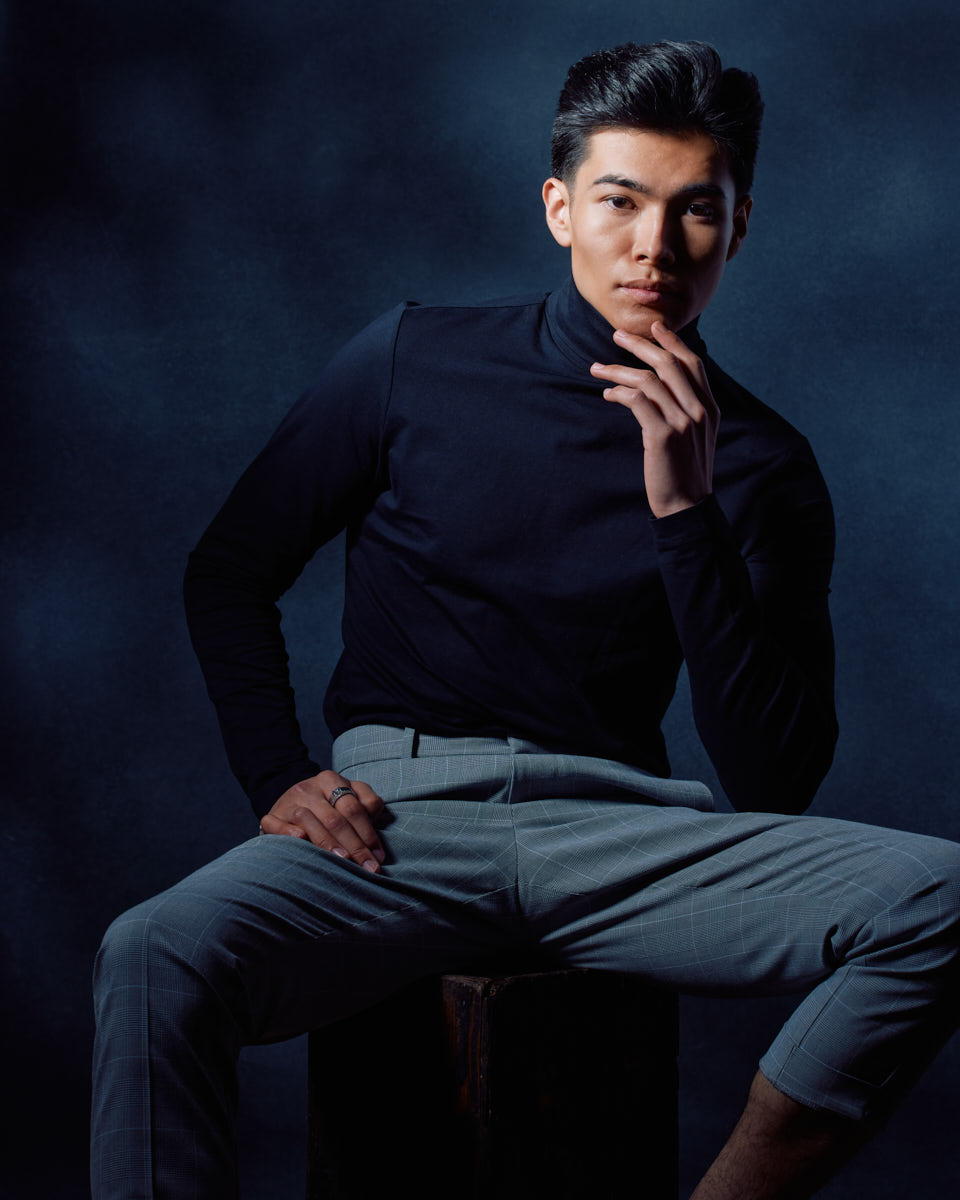 Become a Male Model in Chicago-Santiago is seated, leaning slightly forward with his hand thoughtfully placed near his chin, exuding a contemplative and intense look.