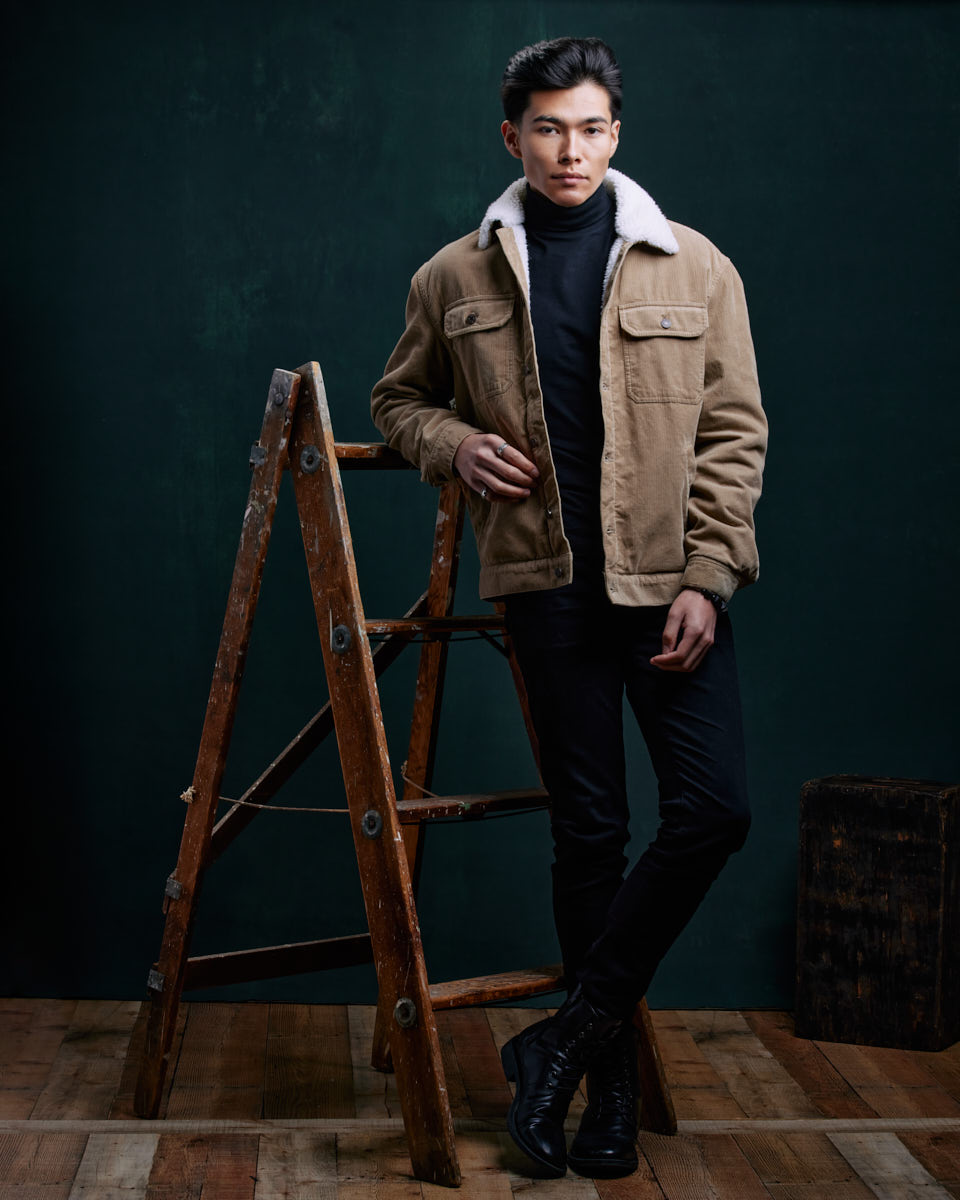 Become a Male Model in Chicago-Santiago stands casually next to a wooden ladder, one hand resting on the ladder while the other is in his pocket, presenting a relaxed yet confident demeanor.