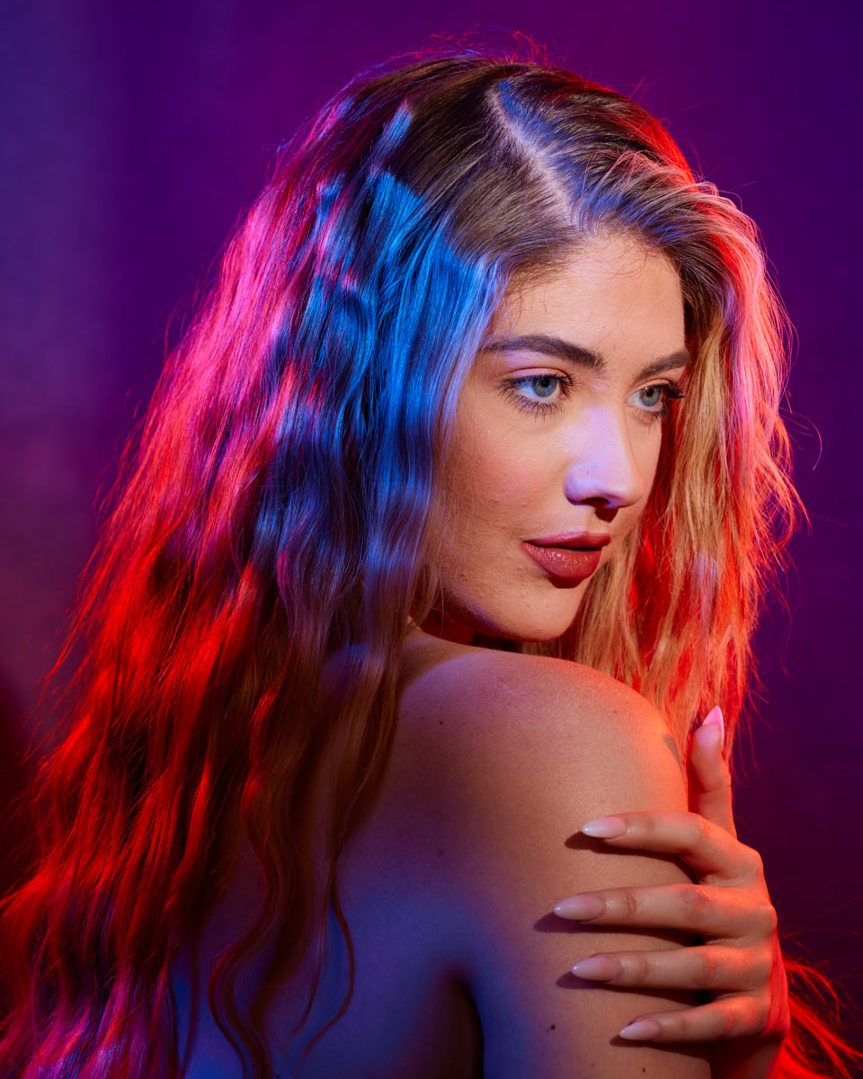Editorial Model Photography in Chicago-A dramatic, close-up side portrait of the model with long wavy hair illuminated by red and blue lights, creating a striking and colorful effect.