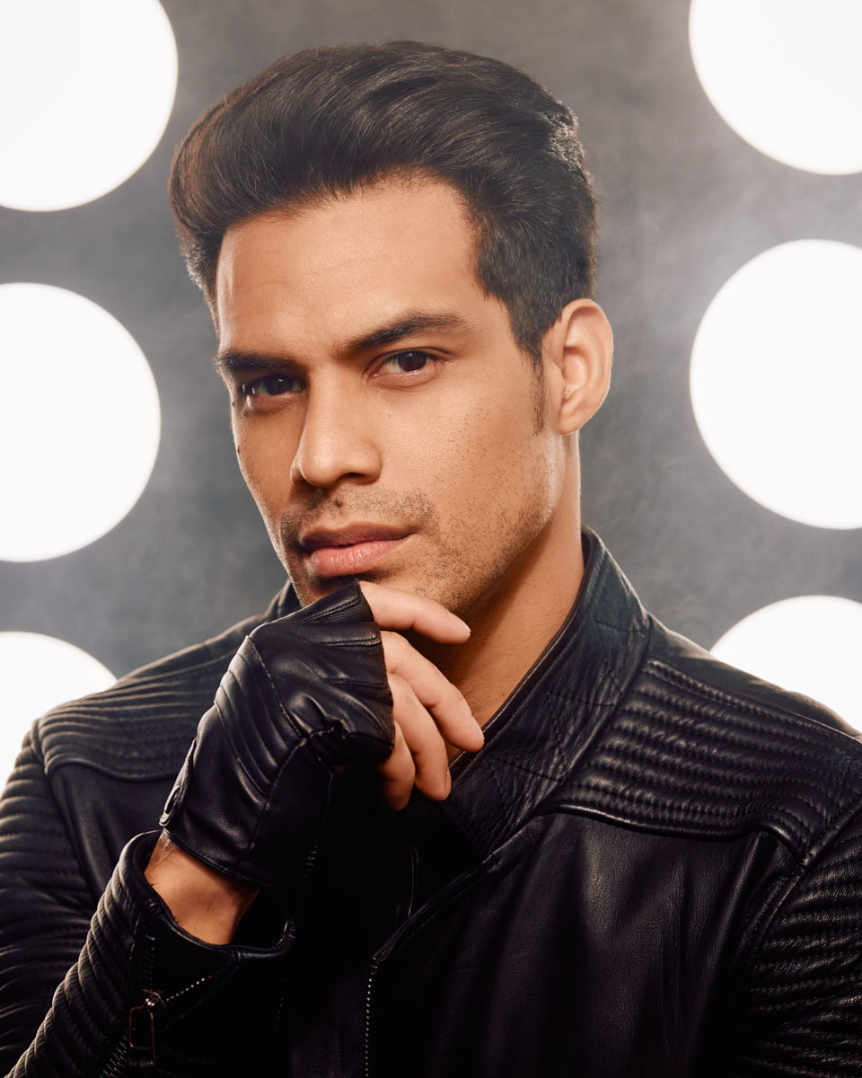 A close-up portrait of the male model, wearing a leather jacket and black gloves, resting his chin on his hand, with a confident expression.