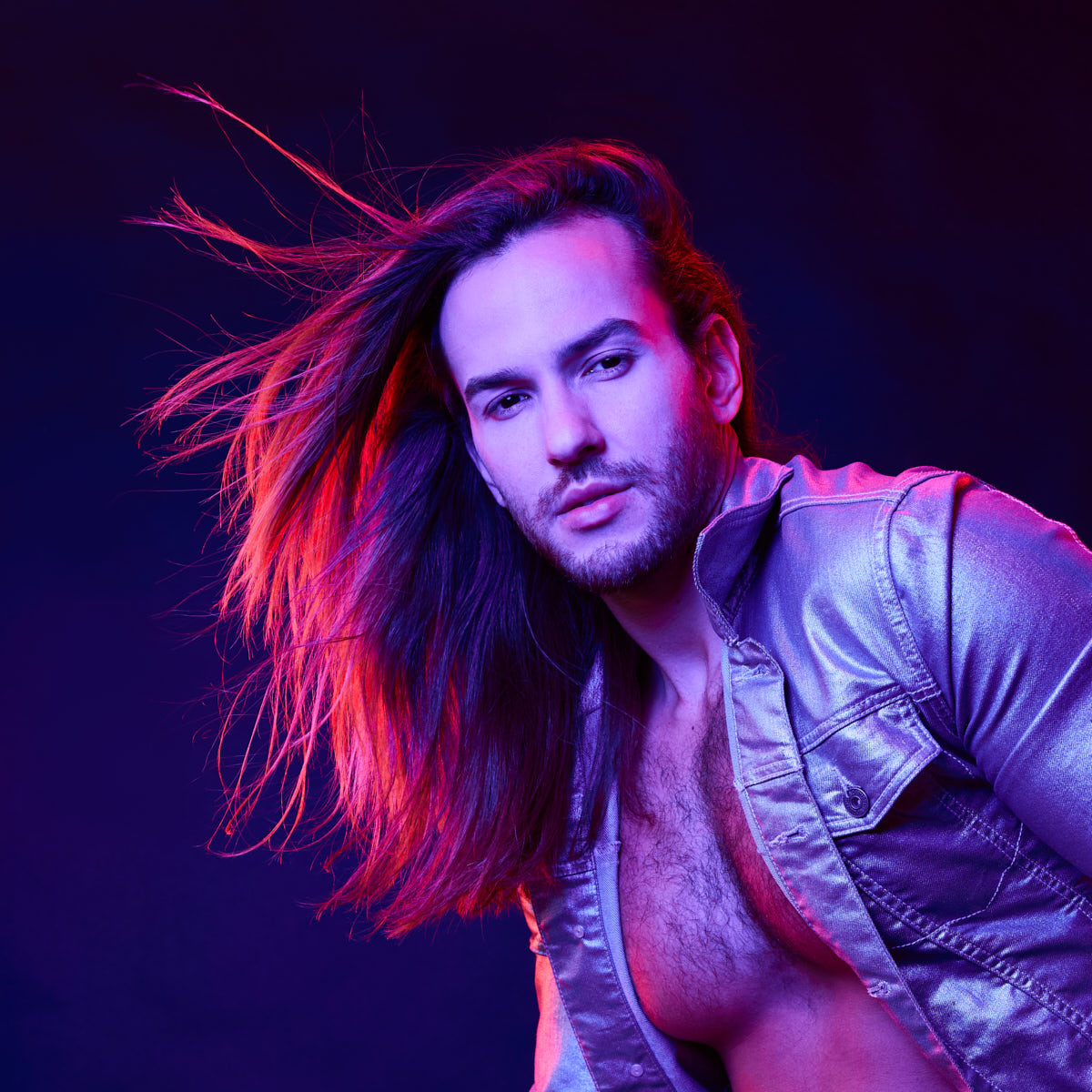 Male Model grooming tips in Chicago-A close-up of Glaydson Jr. with his hair flowing back, highlighting his facial features and expression. The lighting creates a dramatic effect with purple and red tones.