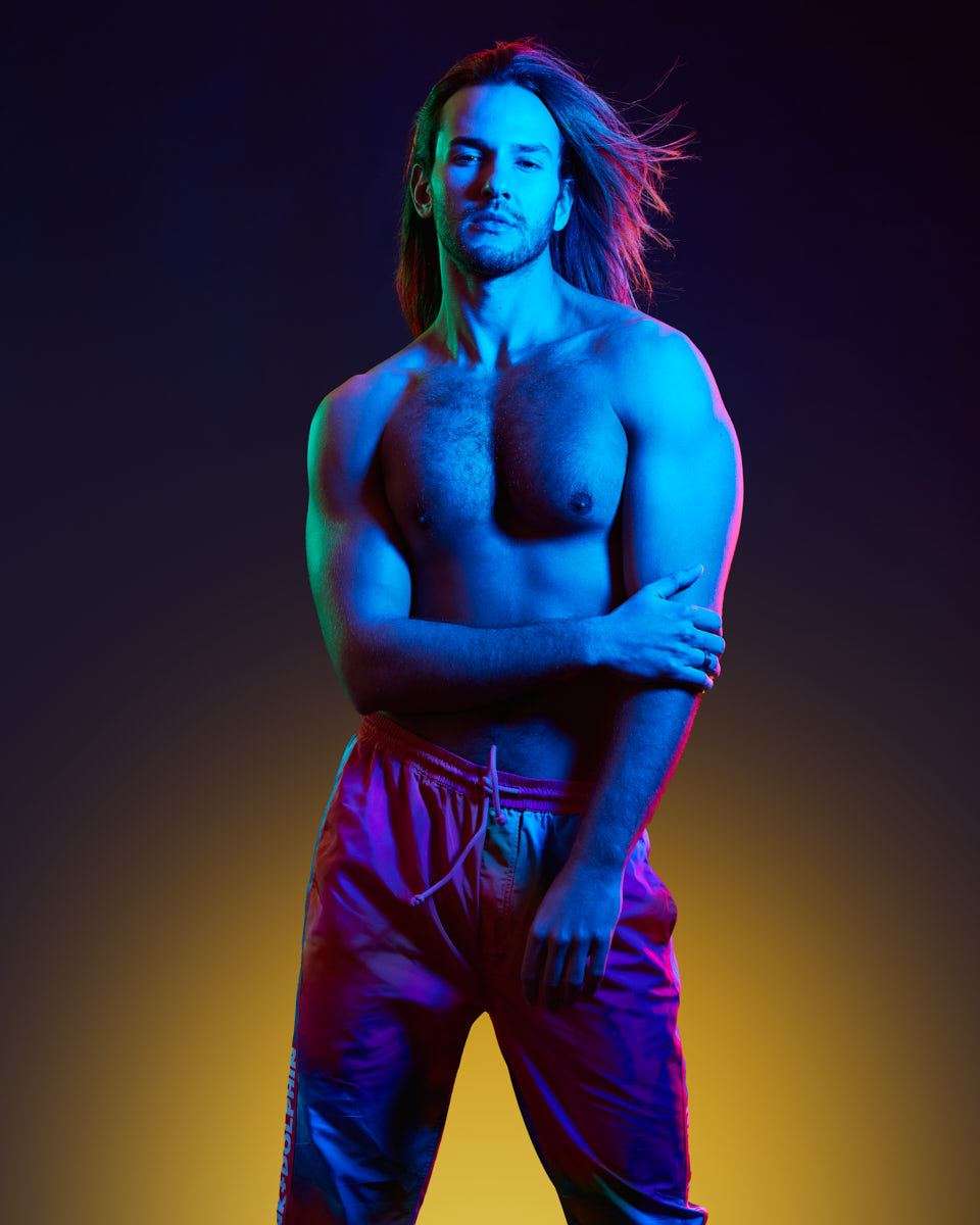 Male Model grooming tips in Chicago-Another full-body shot of Glaydson Jr. in a powerful stance, emphasizing his muscular build and the vibrant lighting that creates a striking contrast.