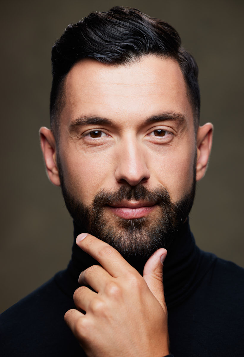 A close-up color portrait of Uros wearing a black turtleneck, with a calm expression and his hand touching his chin.