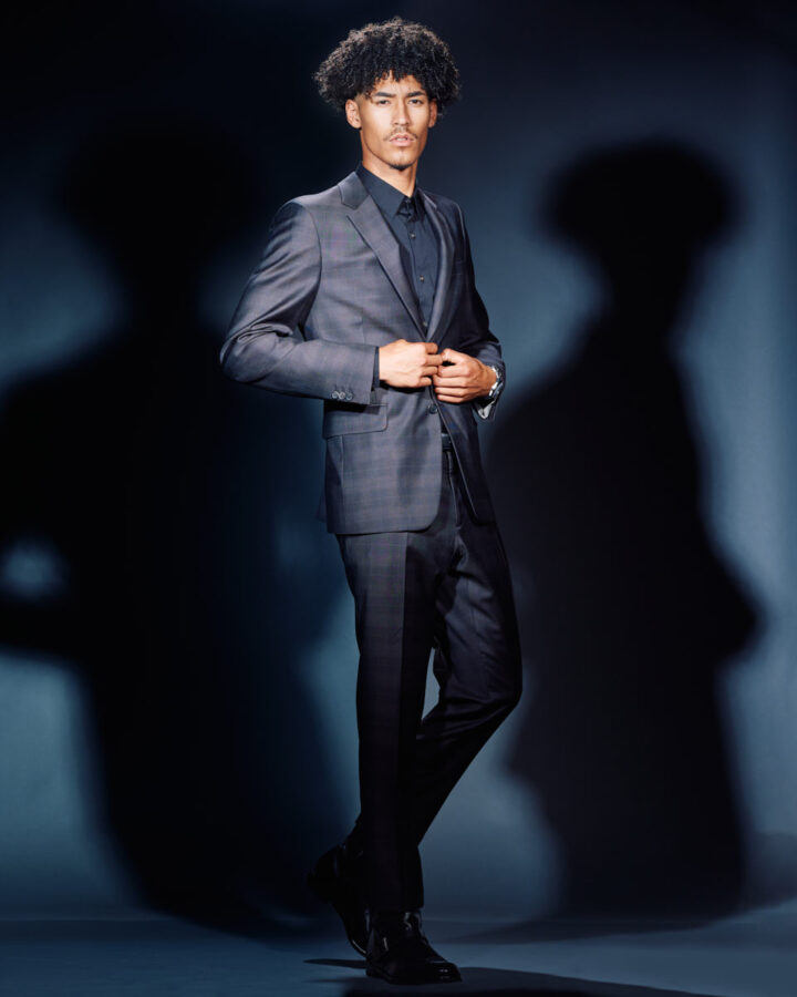 Kasan is dressed in a dark suit, posing against a blue background. The suit is well-fitted, and his expression is serious and professional, adding a sophisticated look to his portfolio.