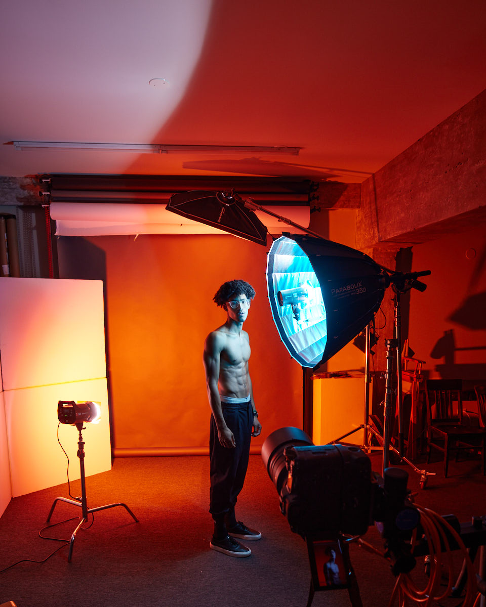 Male modeling portfolio shoot in Chicago-A behind-the-scenes shot of Kasan standing in a studio setup with blue and red lighting. Various photography equipment and light modifiers are visible, showcasing the creative environment of the shoot.