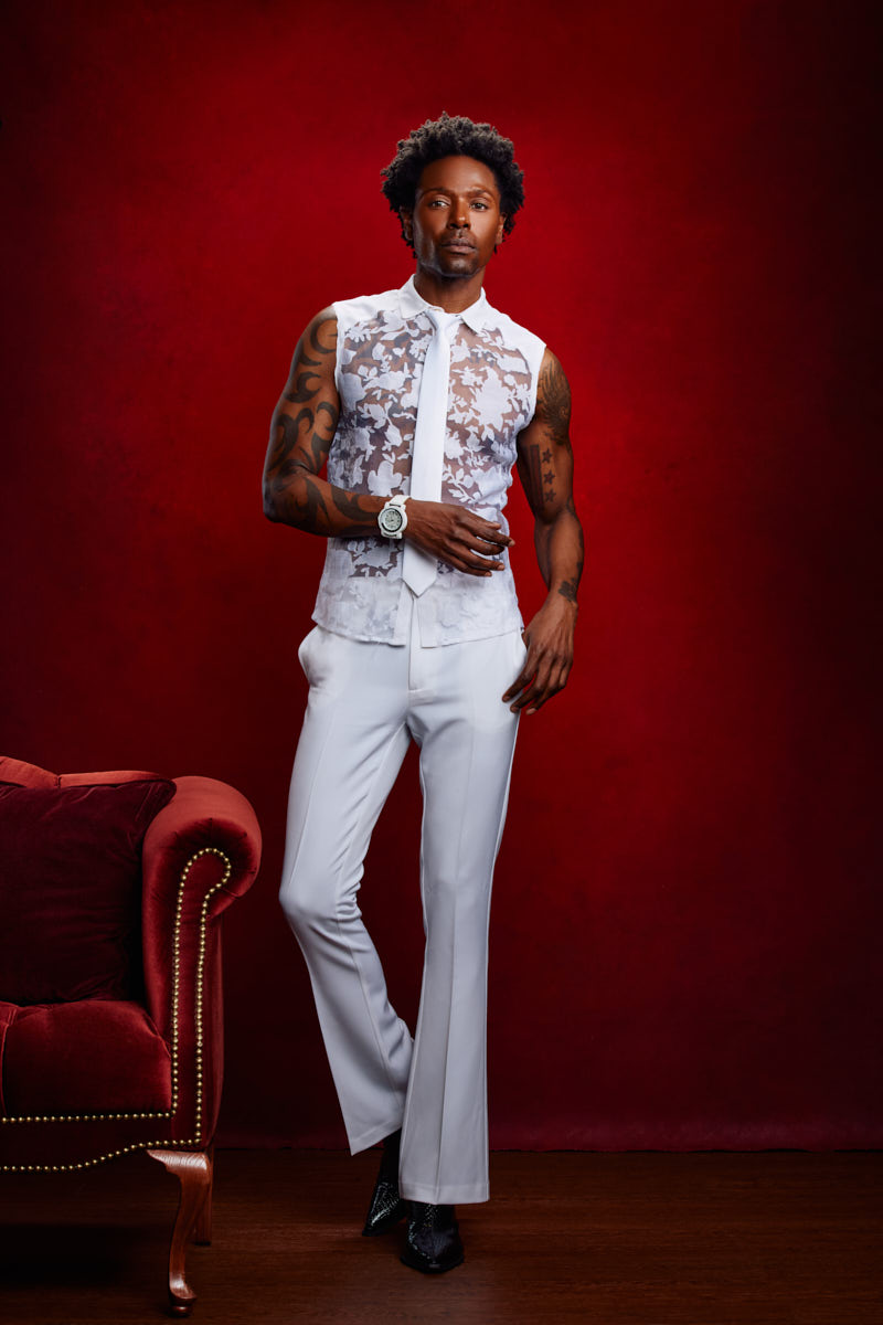 Chris confidently posing in a white lace-patterned outfit during a fashion photoshoot with John Gress.