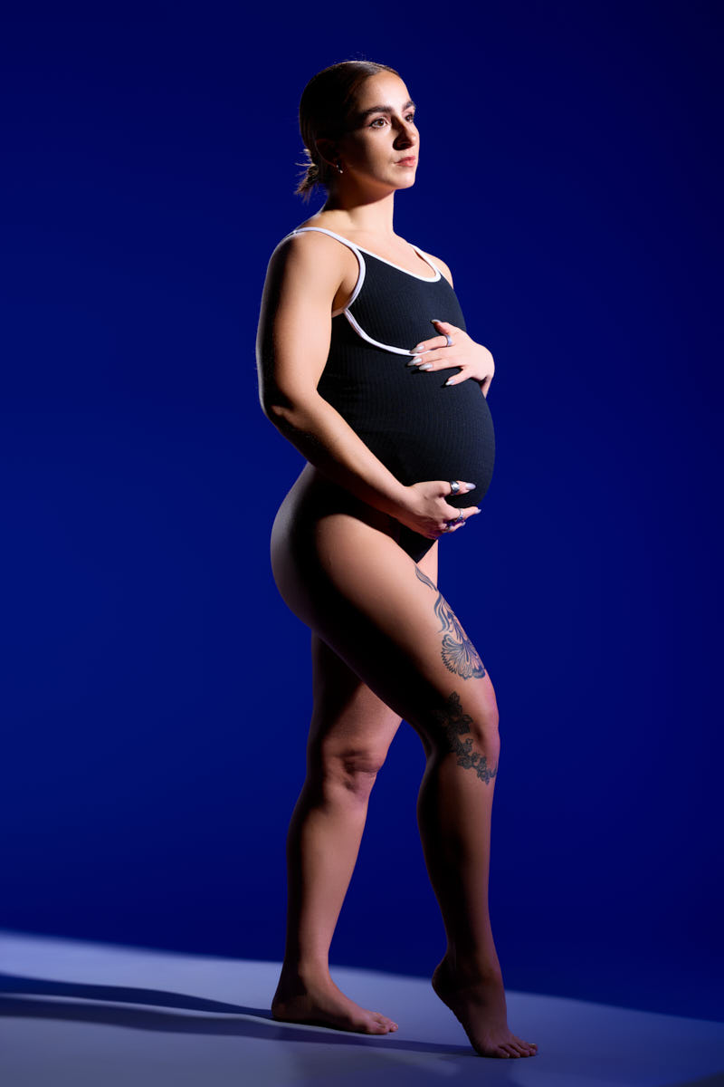 Chicago Maternity Photographer-A glamorous maternity portrait of a woman in an off-the-shoulder black dress with a thigh-high slit, posed confidently.