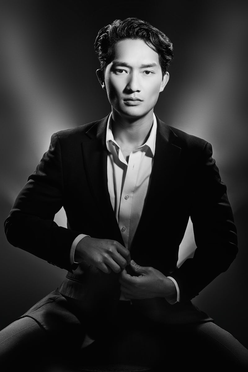 Male Model Poses in Chicago-A classic, sophisticated black and white portrait of a male model wearing a suit. He sits confidently, fastening his jacket with a focused, self-assured expression. The background is clean and dramatic, emphasizing his strong jawline and timeless style.