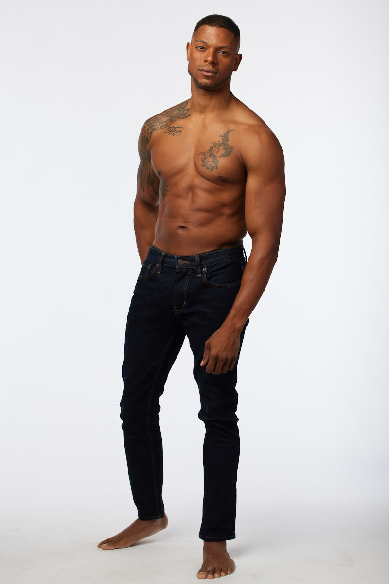 Full-length standing portrait in jeans, relaxed stance with bare feet.