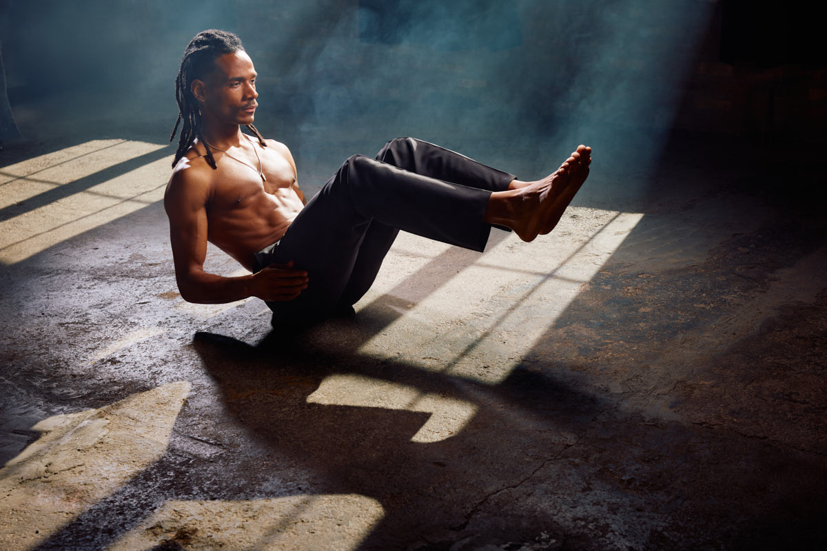 Athletic male in a supported floor pose demonstrating core stability and balance in a dramatic studio setting