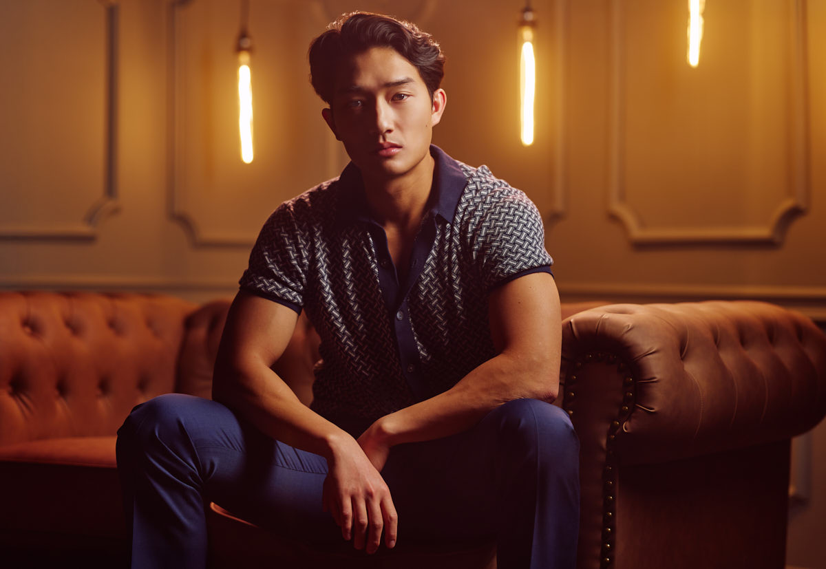 editorial portrait of model Kyle seated on leather sofa with warm lighting