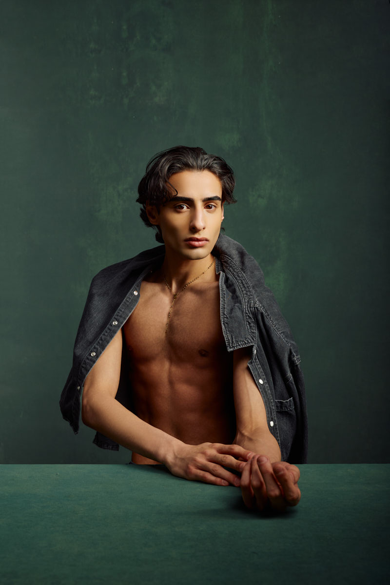 Fashion portrait of Giorgio with a denim jacket draped over his shoulders in a dramatic studio setting.