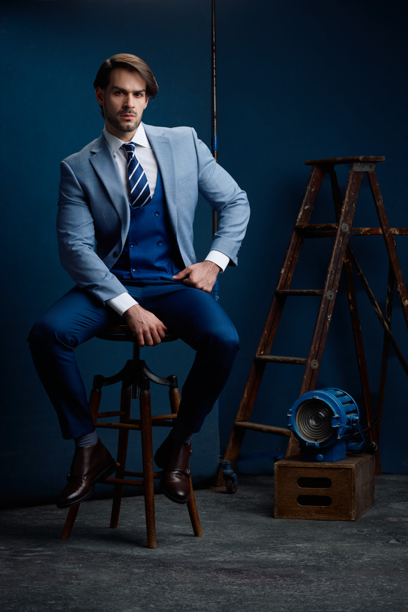 Jamie leans forward on a wooden stool in blue tailoring during an editorial menswear portfolio session.