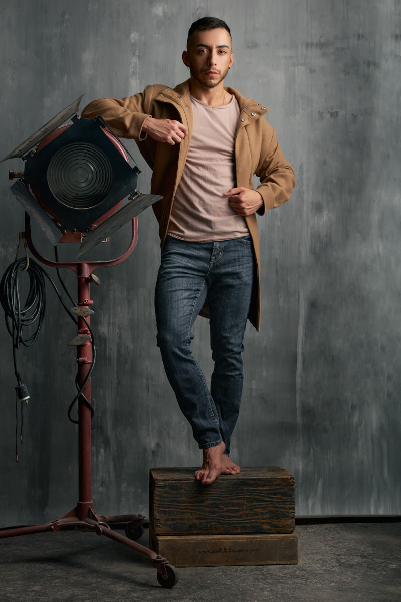 Gael wears a tan jacket and jeans beside a large studio spotlight.