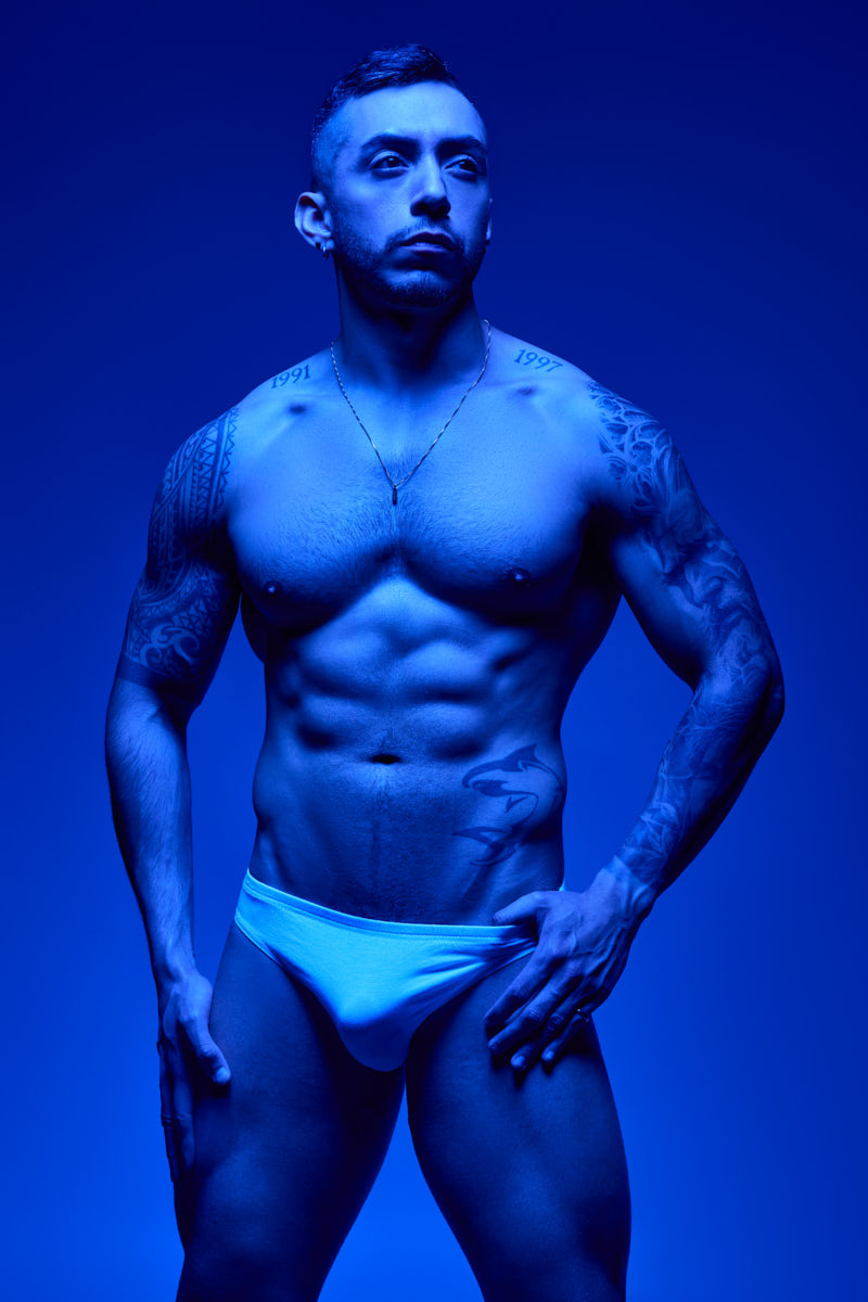 Blue light falls across Gael's torso as he poses in white briefs.