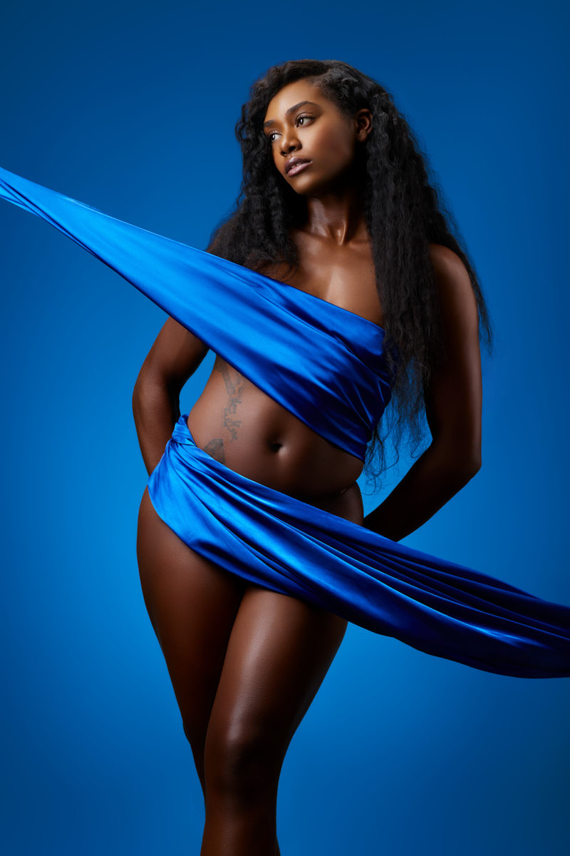 Oneka turns her shoulders in blue draped fabric against a blue studio backdrop.