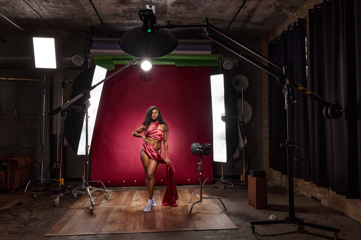 A wide studio view shows Oneka in rose-colored fabric between lights against a burgundy backdrop.