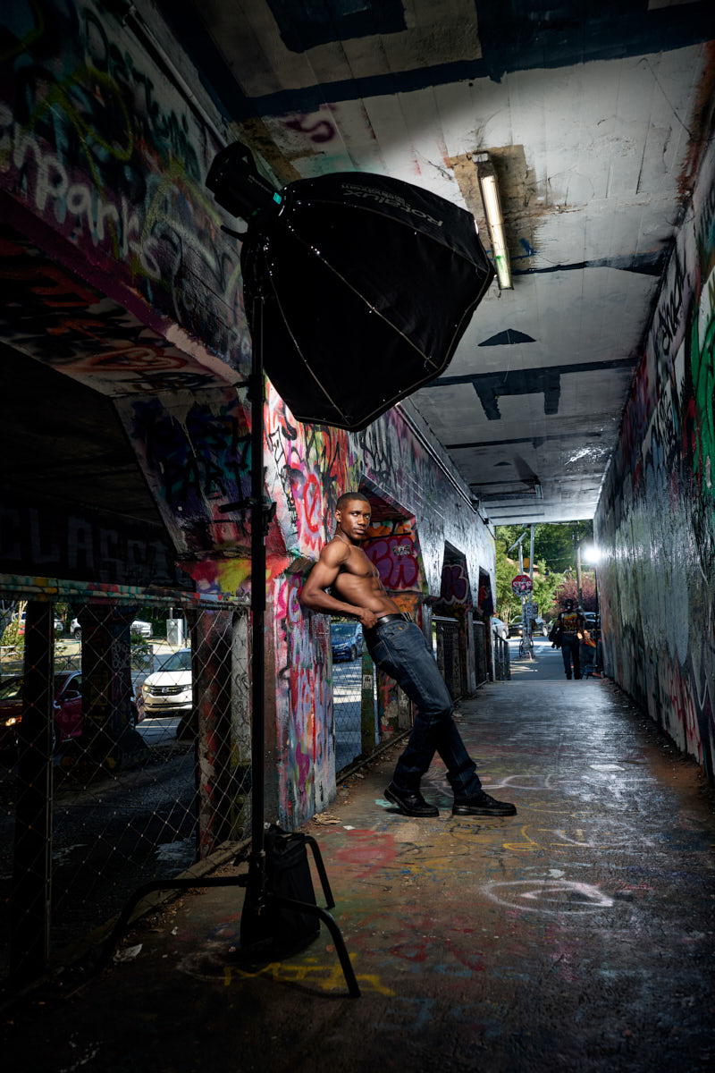 Behind the scenes, Grant poses in a graffiti-covered passage beside a large light modifier.